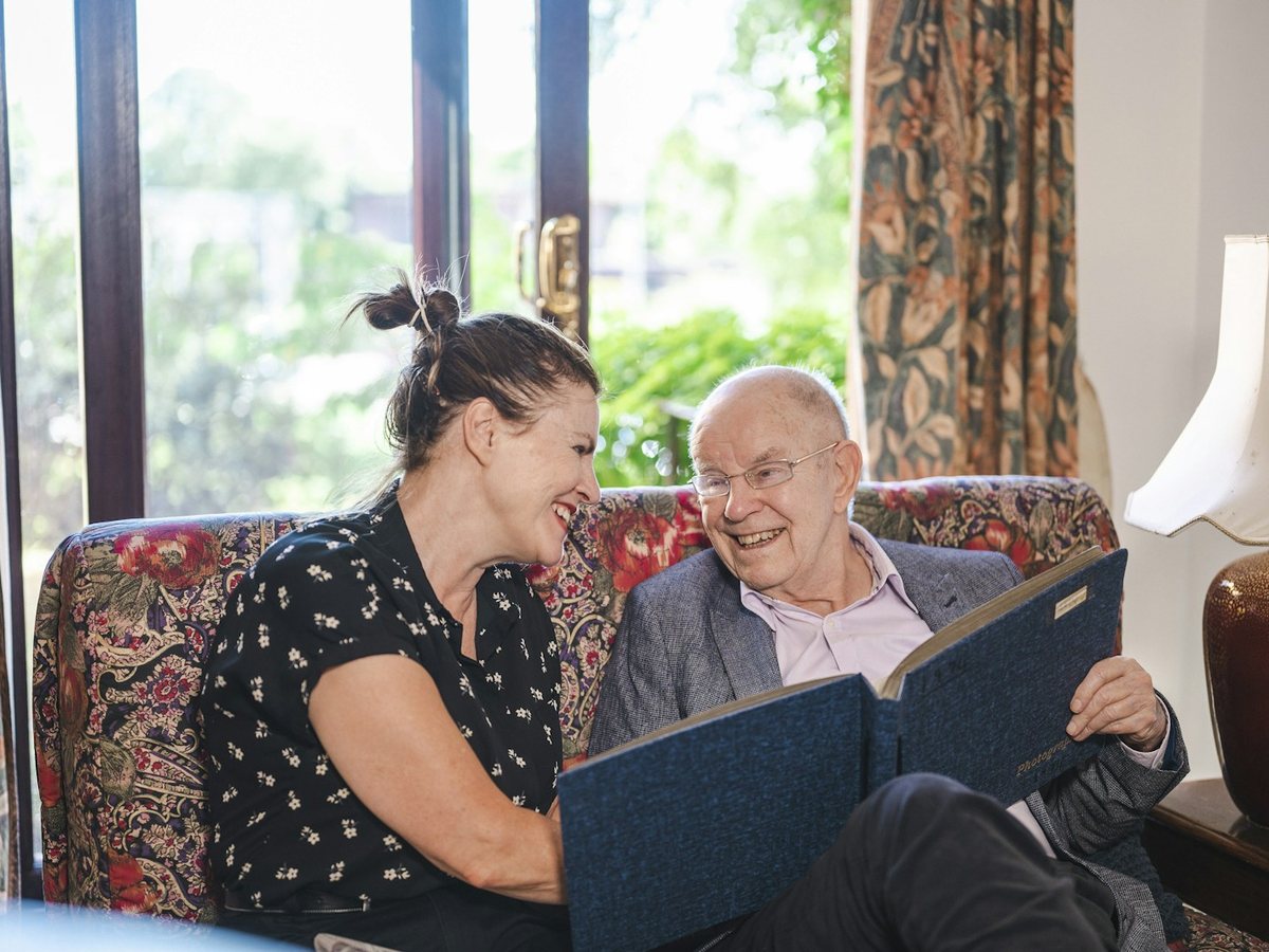 Caregiver sharing a photo album with an older man in his living room