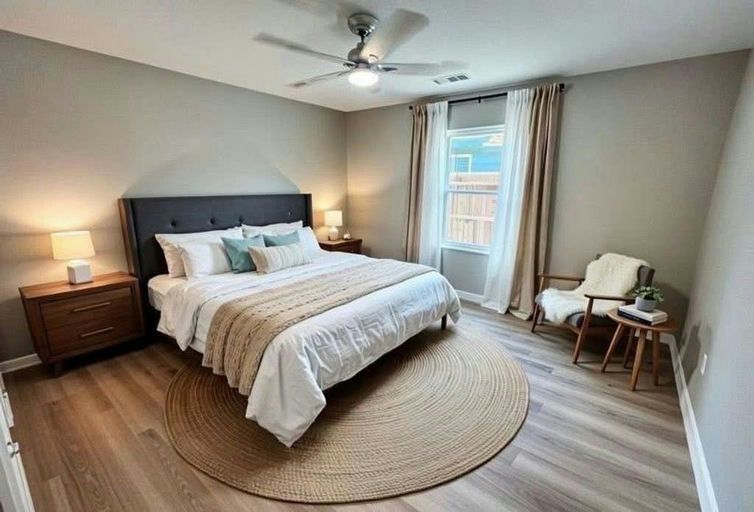 A furnished bedroom with a made bed, nightstand and reading chair