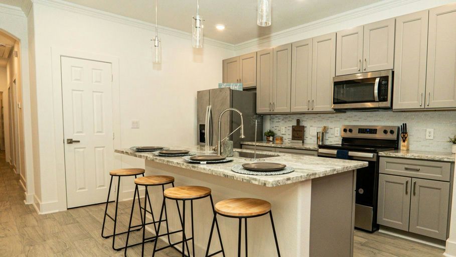 A modern kitchen with gray cabinets, stainless appliances and bar stools at an island