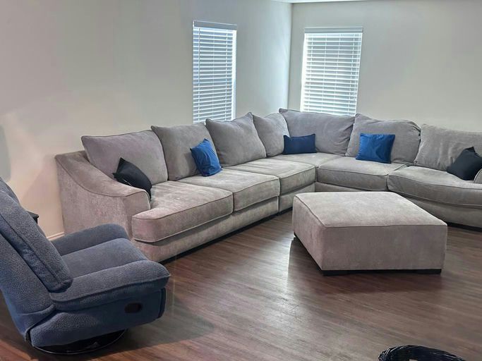 A calm living room with a large gray sectional sofa, ottoman and recliner