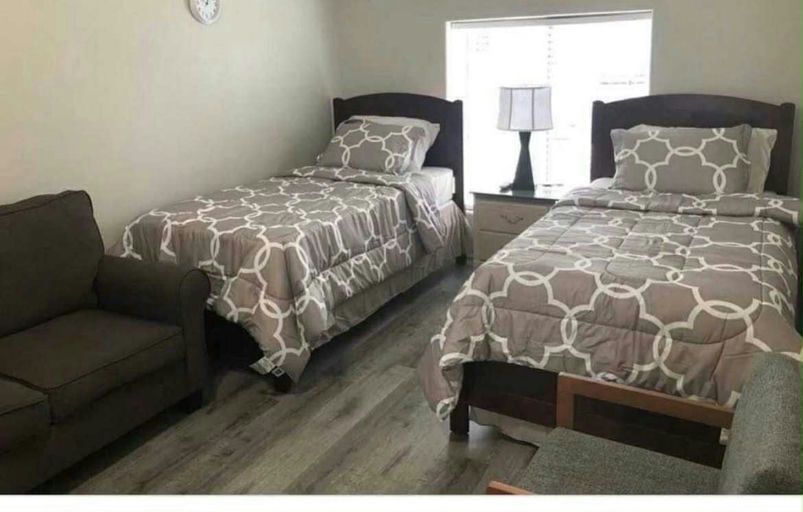 A furnished shared bedroom with two twin beds, an armchair and two lamps